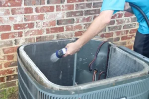 HEARTLAND HEATING & COOLING - A homeowner rinsing the inside of their outdoor air conditioning unit with a hose to help clean it and get it ready for the summer season in Springfield, IL.