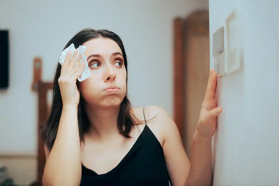 Woman in Springfield, IL, wiping sweat from her forehead while checking her thermostat due to an air conditioner not working properly.